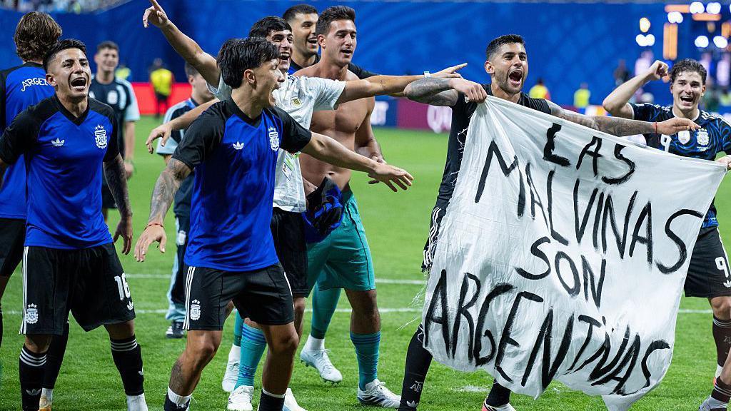 ผู้เล่นทีมชาติอาร์เจนตินากำลังชูธงที่มีข้อความว่า "Las Malvinas son Argentinas"