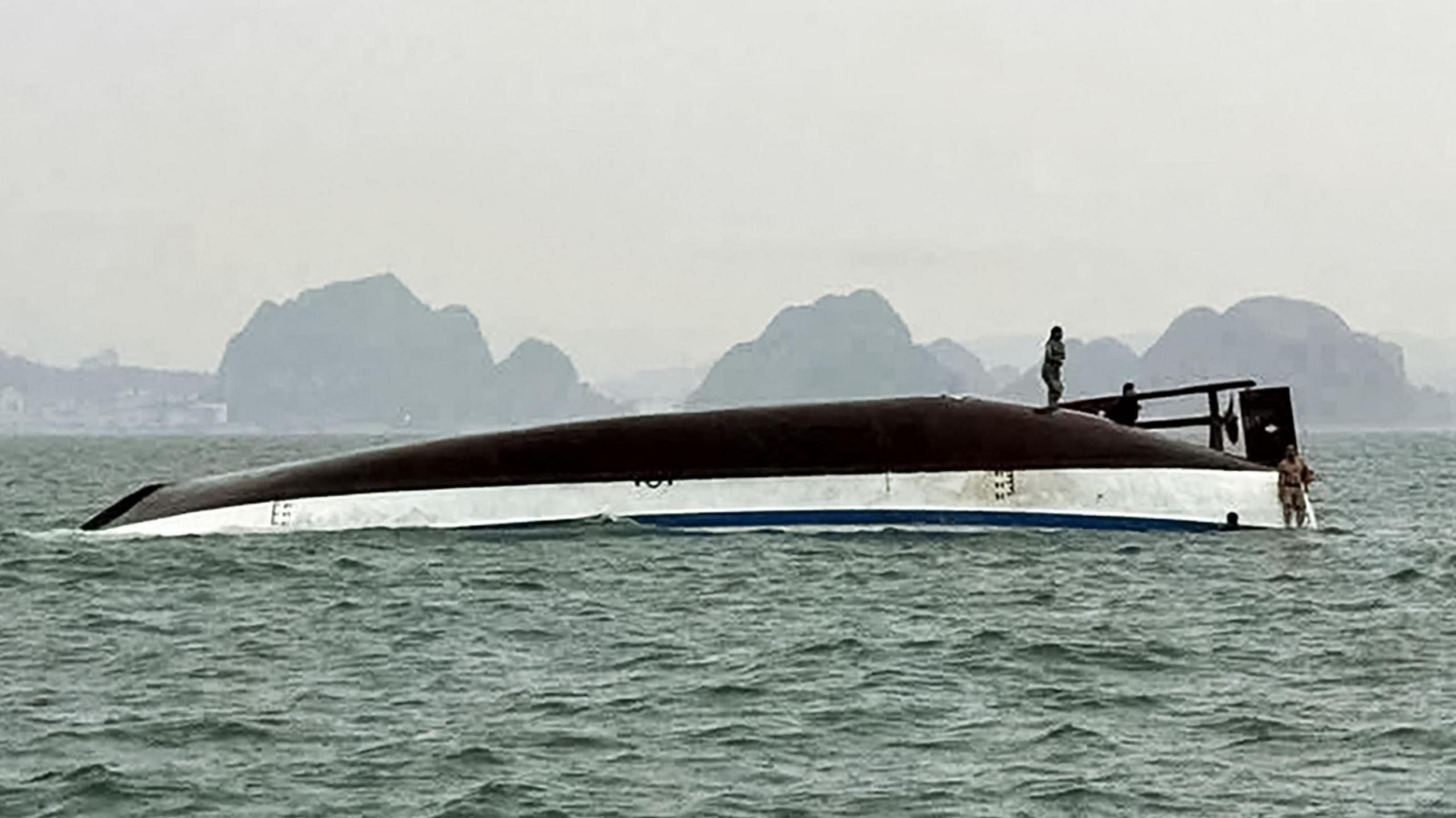 ชายคนหนึ่งยืนอยู่บนเรือท่องเที่ยวที่พลิกคว่ำในอ่าวฮาลอง
