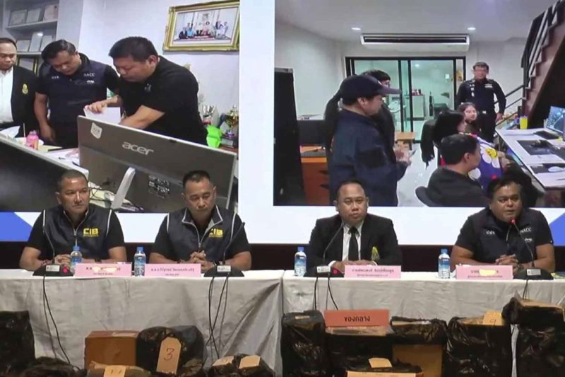 เจ้าหน้าที่บังคับใช้กฎหมายกำลังจัดการแถลงข่าว โดยมีภาพจากปฏิบัติการบุกเข้าตรวจค้นบ้านในจังหวัดนนทบุรี ที่เจ้าหน้าที่รัฐหลายคนถูกจับได้ว่ากำลังแก้ไขกระดาษคำตอบสอบ ได้รับการฉายขึ้นบนจอขนาดใหญ่ ที่สำนักงานคณะกรรมการป้องกันและปราบปรามการทุจริตแห่งชาติเมื่อเดือนที่แล้ว (ภาพหน้าจอ)