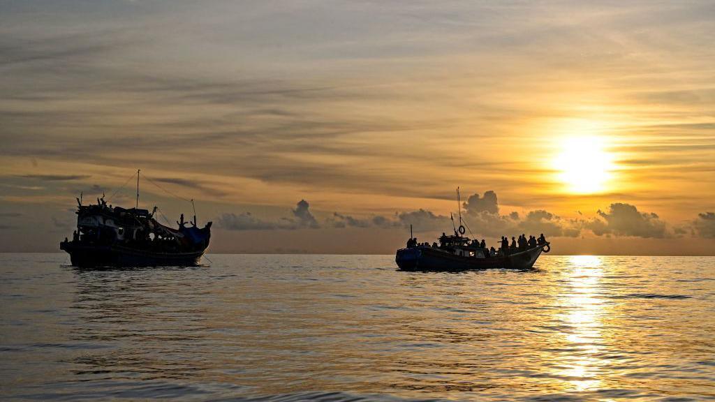 เรือสองลำบรรทุกผู้คนจำนวนมากกำลังลอยอยู่ในทะเลท่ามกลางแสงอาทิตย์ยามอัสดง