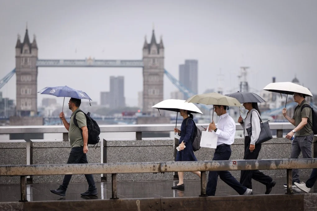 ผู้คนเดินทางข้ามสะพานลอนดอนท่ามกลางฝนตกหนักในอังกฤษเมื่อวันพฤหัสบดี ภาพ: EPA