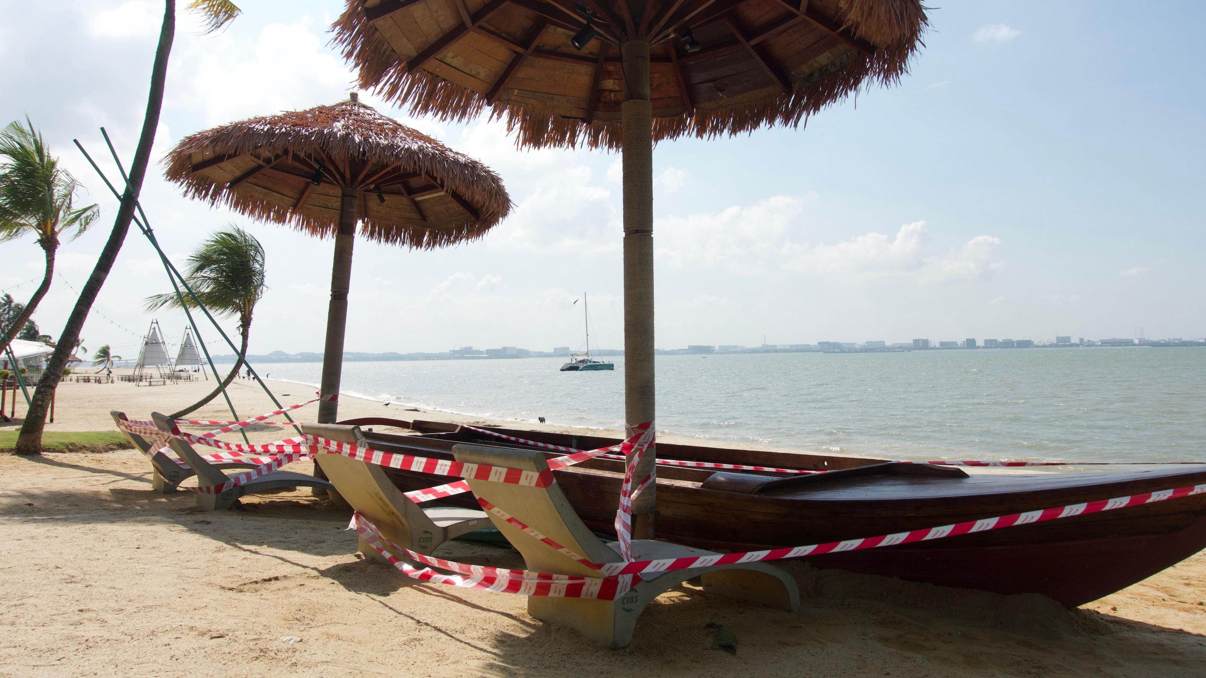 เรือไม้ที่ดัดแปลงเป็นม้านั่งริมหาด ใต้ร่มใยปาล์ม และข้างเก้าอี้หินรูปกล้วย พันด้วยเทป