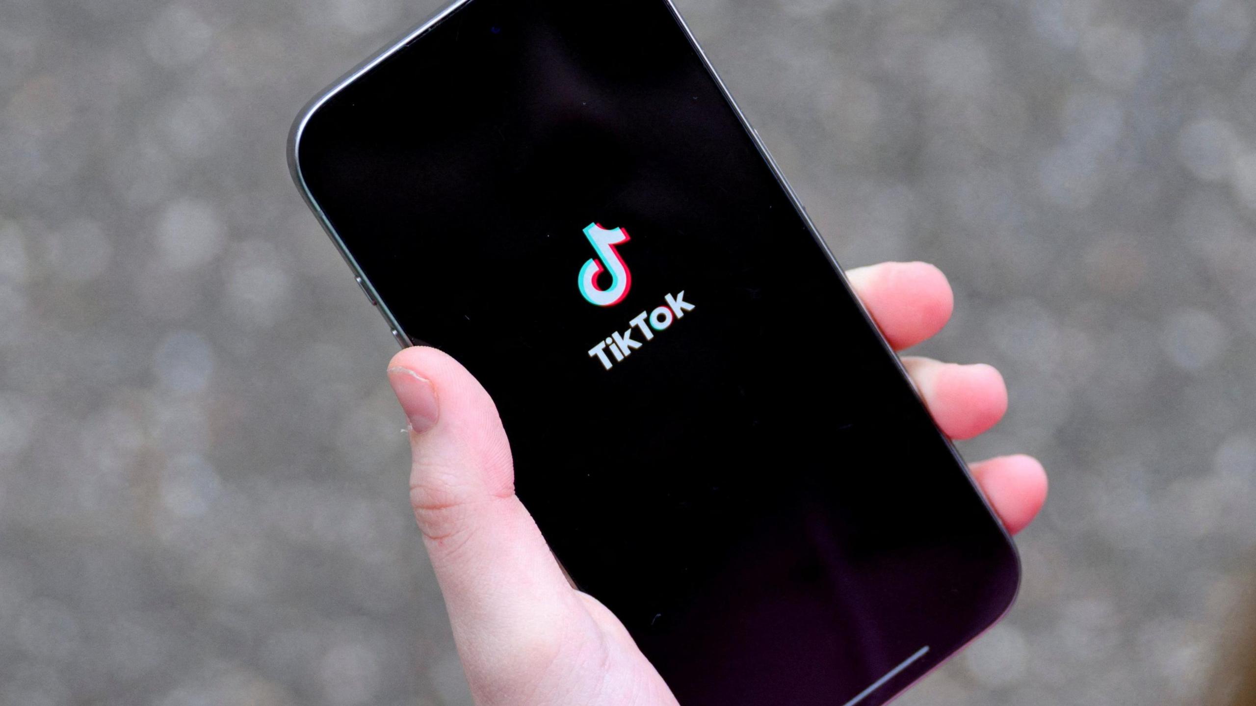 หญิงสาวกำลังถือ iPhone พร้อมแสดงแอปพลิเคชัน TikTok
