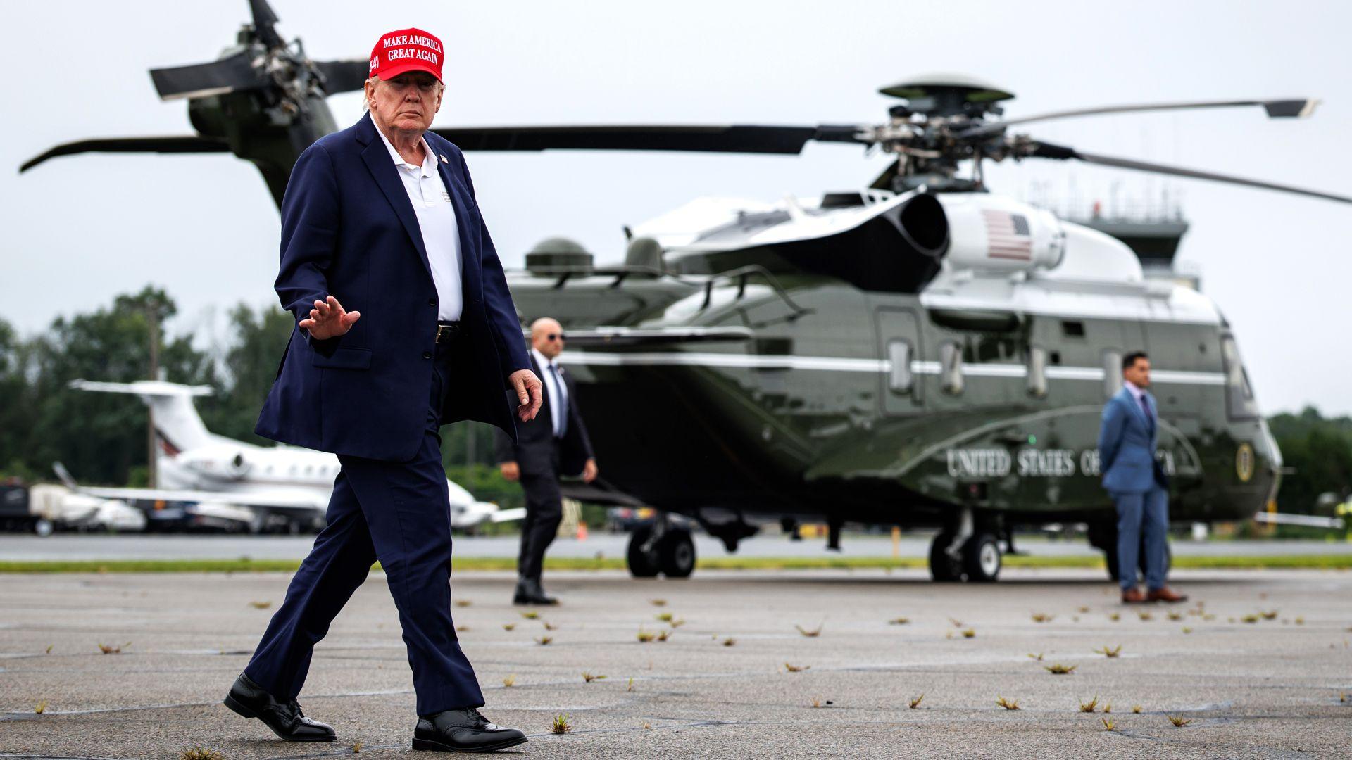 ทรัมป์สวมหมวก MAGA สีแดง กำลังเดินอยู่หน้าเฮลิคอปเตอร์ Marine Force One และโบกมือ