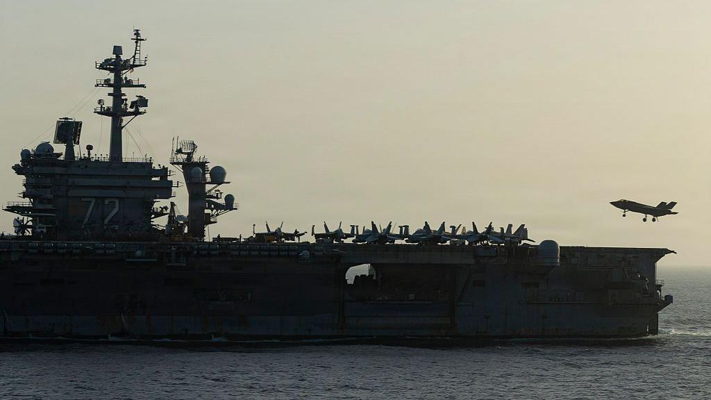 ภาพด้านข้างของเรือ USS Abraham Lincoln ขณะที่เครื่องบินไอพ่นขนาดเล็กกำลังลงจอด