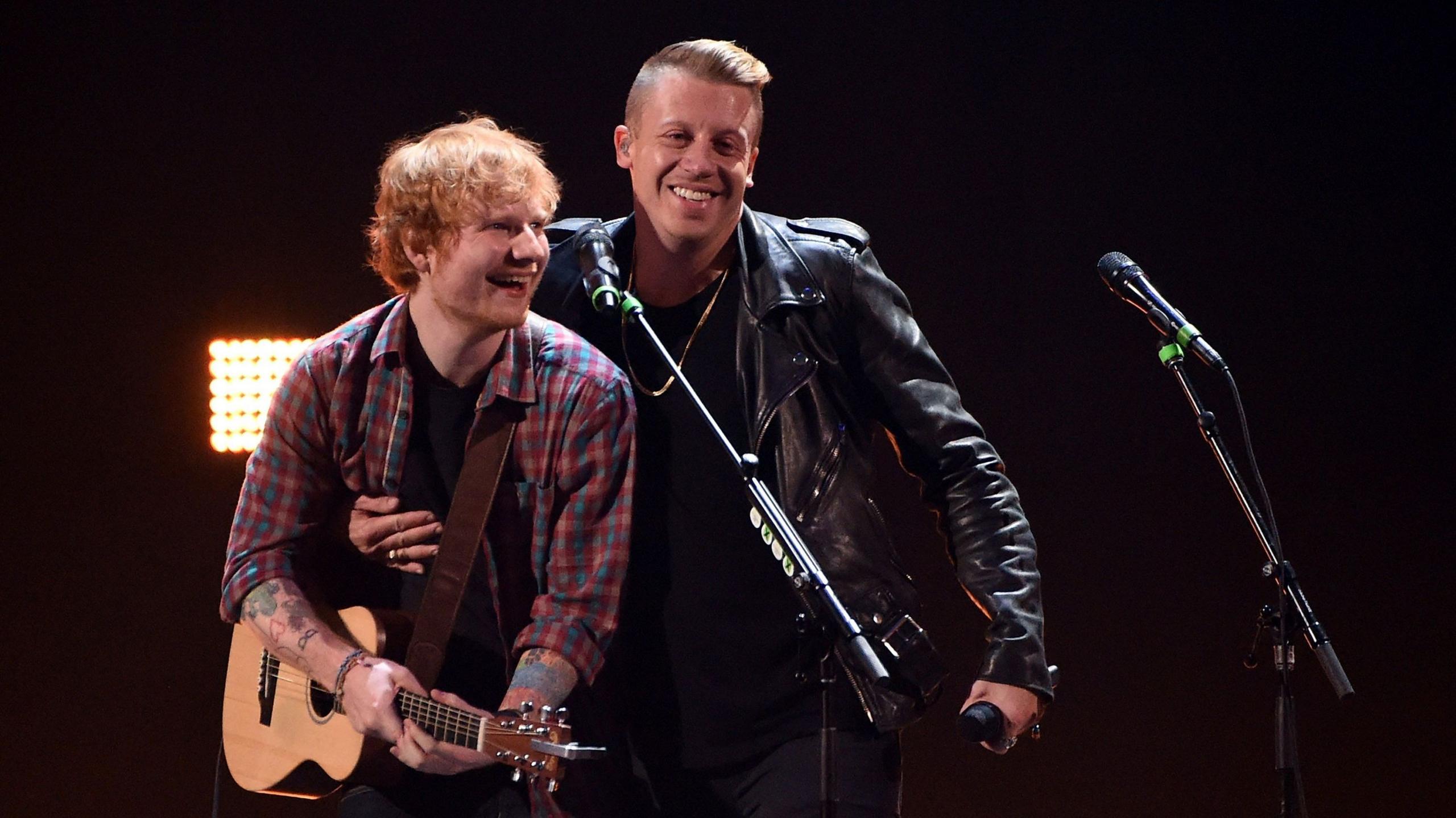 นักร้อง/นักแต่งเพลง Ed Sheeran (ซ้าย) และแร็ปเปอร์ Macklemore แสดงสดในงาน iHeartRadio Music Festival ปี 2014 ที่ MGM Grand Garden Arena เมื่อวันที่ 20 กันยายน 2014 ที่ลาสเวกัส รัฐเนวาดา Sheeran สวมเสื้อเชิ้ตลายตารางและกำลังถือกีตาร์ ส่วน Macklemore สวมแจ็กเก็ตสีดำ