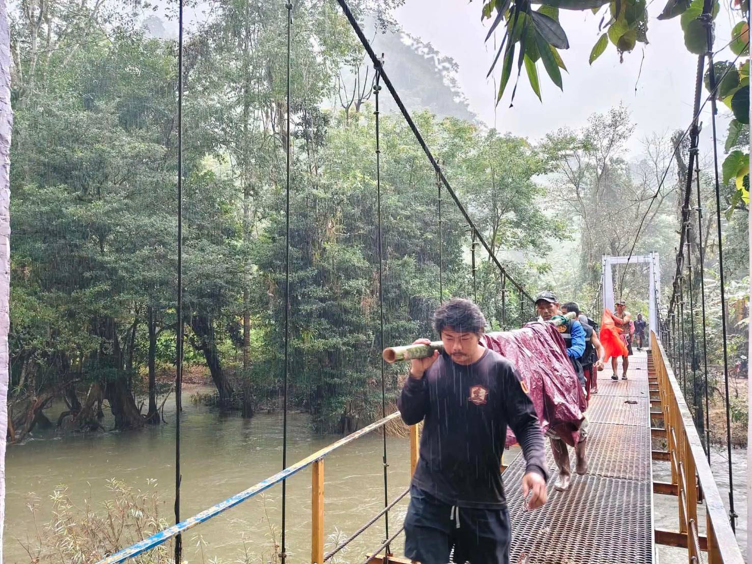 อาสาสมัครแบกคุณยายเสพือยข้ามสะพานท่ามกลางสายฝน (ภาพ: ปิยะราช จงเจริญ)