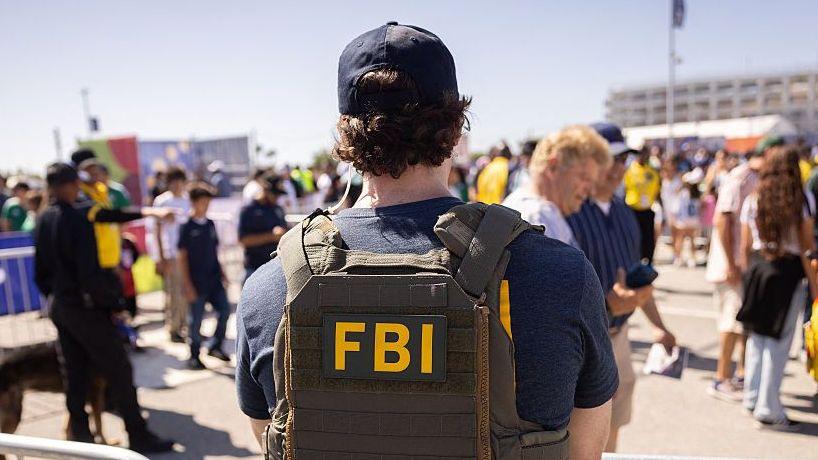 เจ้าหน้าที่ FBI ยืนอยู่ใกล้จุดรักษาความปลอดภัยที่สนามกีฬาลอสแอนเจลิส (SoFi Stadium) ก่อนการแข่งขันฟุตบอลโลก 2026 รอบแบ่งกลุ่ม กลุ่ม G ระหว่างอิหร่านกับนิวซีแลนด์ในเมืองอิงเกิลวูด รัฐแคลิฟอร์เนีย เมื่อวันที่ 15 มิถุนายน 2026