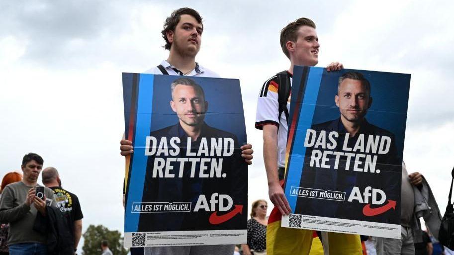 ผู้สนับสนุนพรรค Alternative for Germany (AfD) ถือป้ายขณะเข้าร่วมกิจกรรมหาเสียงของผู้สมัครอันดับหนึ่งของพรรค AfD อุลริช ซีกมุนด์ ก่อนการเลือกตั้งระดับรัฐซัคเซิน-อันฮัลต์ ที่จะมาถึงในเมืองมักเดบูร์ก ประเทศเยอรมนี