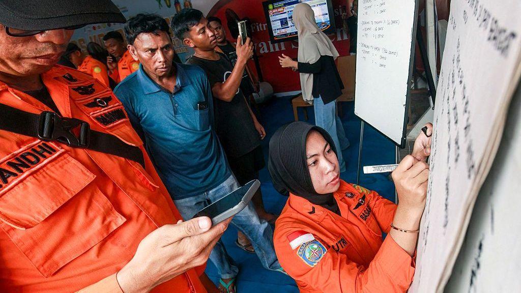 ญาติของผู้โดยสารที่ได้รับผลกระทบเฝ้าดูเจ้าหน้าที่จากหน่วยงานค้นหาและกู้ภัยแห่งชาติ (Basarnas) เขียนข้อมูลอัปเดตบนไวท์บอร์ด ท่ามกลางปฏิบัติการกู้ภัยที่กำลังดำเนินอยู่บนเรือเฟอร์รีเวอร์โก ทรานสปอร์ต 8 ที่ท่าเรือตริศักดิ์ บันดาร์มาซิน จังหวัดกาลิมันตันใต้ เมื่อวันที่ 13 กันยายน 2026