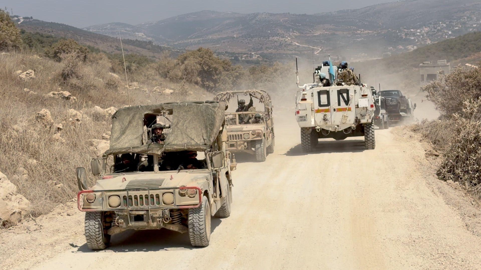 ยานพาหนะทางทหารของอิสราเอลสองคันแล่นผ่านขบวนรถ Unifil บนถนนเลียบกำแพงที่กั้นระหว่างเลบานอนและอิสราเอล