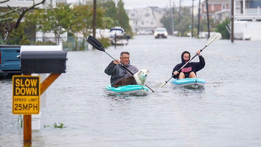 ชายหญิงพายเรือคายัคบนถนนที่ถูกน้ำท่วม โดยมีสุนัขอยู่บนเรือคายัคของชายผู้นั้น
