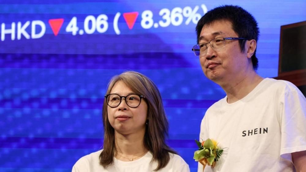 Xu Yangtian ผู้ก่อตั้ง Shein (ขวา) ยืนอยู่บนเวทีข้าง Poppy Bao ผู้อำนวยการฝ่ายการเงิน ในพิธีจดทะเบียนบริษัท ด้านหลังเป็นหน้าจอสีน้ำเงินแสดงราคาหุ้น Shein ลดลง 8.36%.