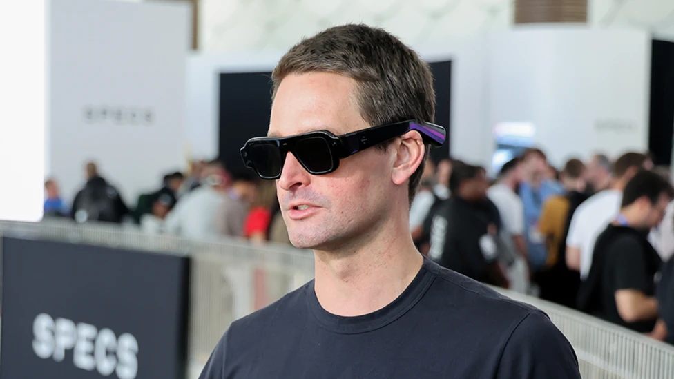 Evan Spiegel, ชายผมสั้น สวมแว่นตาที่คล้ายแว่นกันลมผสมกับแว่นกันแดดทรงนักบินขนาดใหญ่