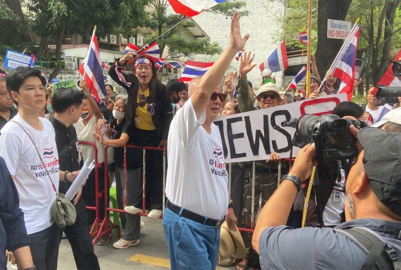 สนธิ ลิ้มทองกุล อดีตแกนนำกลุ่มพันธมิตรฯ และผู้ก่อตั้งเครือผู้จัดการ ทักทายผู้สนับสนุน โดยมีผู้หนึ่งถือป้ายเขียนว่า “Jews Out” ระหว่างการชุมนุมหน้าสถานทูตอิสราเอลในกรุงเทพฯ เมื่อวันพฤหัสบดี (ภาพ: Sondhi Talk Facebook)