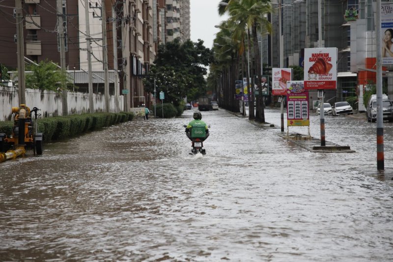 พนักงานส่งอาหารแกร็บขี่รถฝ่าถนนที่ถูกน้ำท่วมในเมืองทองธานี นนทบุรี