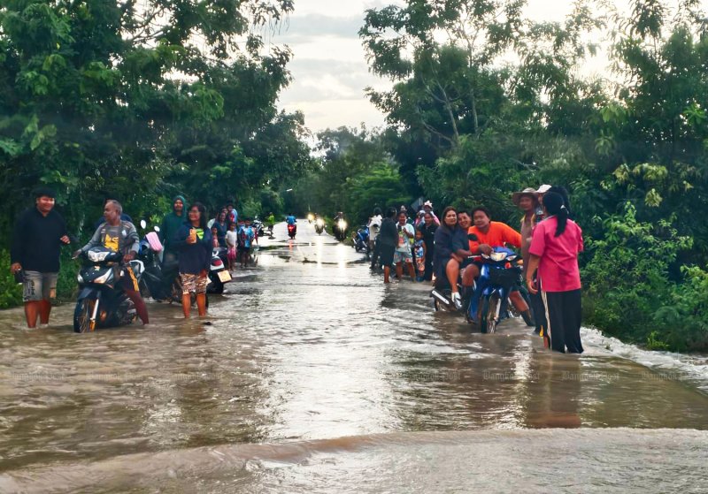 ผู้ขับขี่รถจักรยานยนต์กำลังขับผ่านถนนลาหานทราย–โนนดินแดงในพื้นที่น้ำท่วมขังที่สำโรงใหม่ อำเภอละหานทราย บุรีรัมย์ เมื่อวันพฤหัสบดี (ภาพ: สุรชัย พีระกษา)