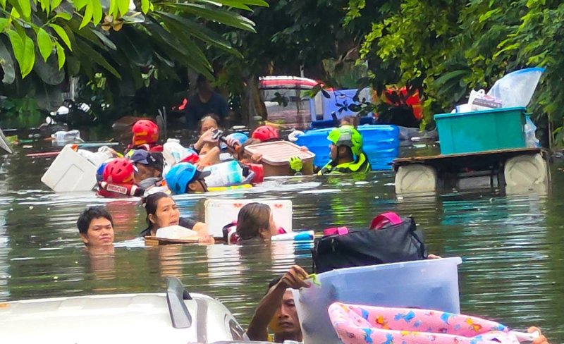 ภาพประชาชนกำลังเดินลุยน้ำที่ท่วมสูงระดับคอ ขณะที่อาสาสมัครมูลนิธิป่อเต็กตึ๊งอพยพผู้ที่ติดค้างและผู้เปราะบางออกจากโครงการเคหะร่มเกล้า เขตลาดกระบัง เมื่อวันอาทิตย์