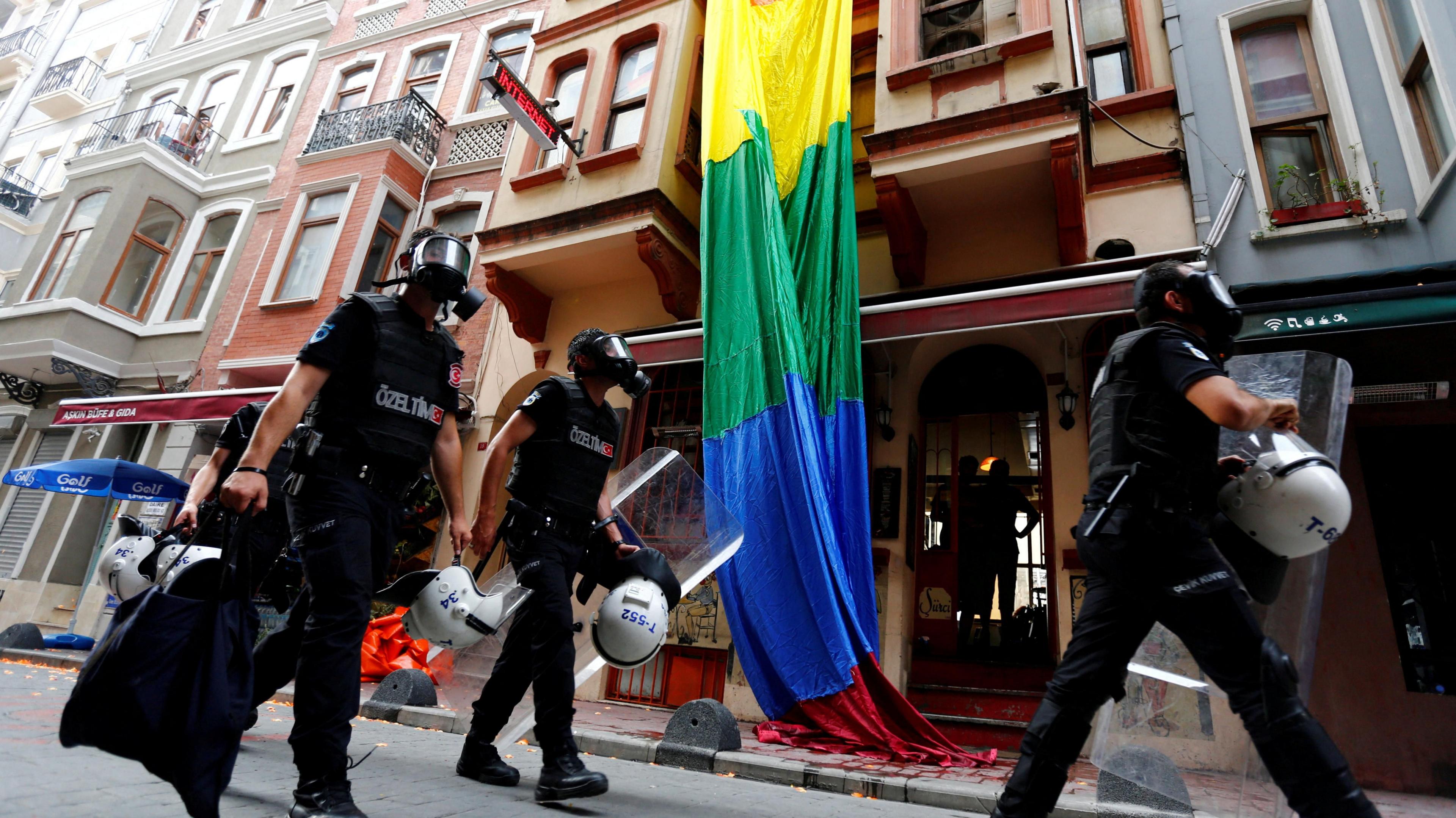 ตำรวจปราบจลาจลพร้อมธงสีรุ้งไล่ตามนักเคลื่อนไหว LGBT ที่พยายามรวมตัวกันเพื่อเดินขบวนไพรด์ซึ่งถูกผู้ว่าการอิสตันบูลสั่งห้าม เจ้าหน้าที่ในชุดเครื่องแบบสีดำ สวมหน้ากากแก๊ส สวมหมวกกันน็อค และถือโล่ปราบจลาจล เคลื่อนที่ไปตามถนนที่ดูเหมือนจะเป็นถนนที่อยู่อาศัย