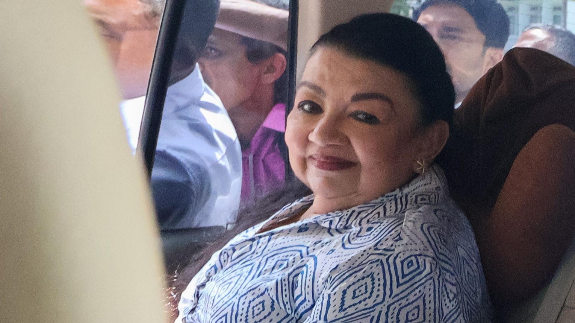 เชียรานตี ราชปักษา นั่งอยู่ในรถและมองตรงมายังกล้อง เธอสวมเสื้อเชิ้ตสีขาวลายเรขาคณิตสีน้ำเงิน ขณะที่มีผู้คนอยู่บนถนนปรากฏให้เห็นผ่านกระจกรถ